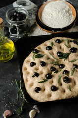 Cooking focaccia bread. Raw focaccia with ingredients on the table, olives, rosemary.