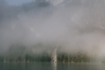 views of forest among fog in border of the lake with a waterfall