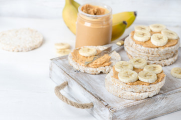 Healthy breakfast with rice cakes with peanut butter and slices of banana on white wooden table