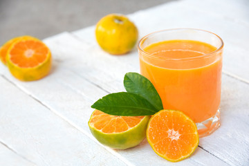 a glass of orange juice and fresh oranges on white wooden base