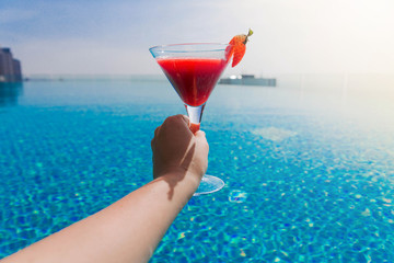 A glass of strawberry cocktail in female hands. Swimming pool