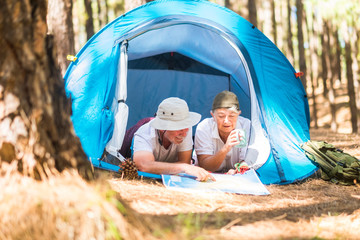 Caucasian traveler adult couple lay down inside a tent while choose and plan on a map the next step of their journey - nature lifestyle leisure activity for alternative retired people