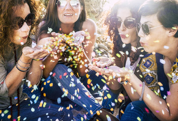 Group of attractive middle age young women playing and blowing out a lot of coloured confetti in...
