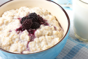 Healthy breakfast with a glass of milk, homemade oatmeal with blackberries in a blue bowl and fresh cereal bread on a light background