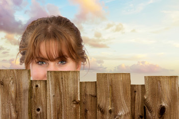 Junge Frau steht versteckt hinter einem Zaun