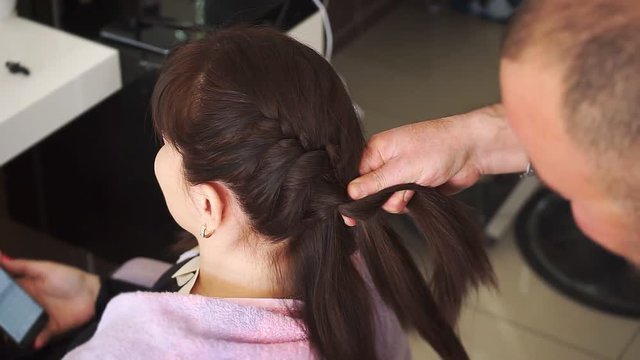 Male hands of master braid hair of young girls