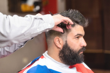 Handsome bearded man, having hair cut by scissors at barber shop .