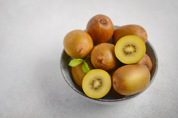 Yellow kiwi fruit in a bowl on a gray concrete background, selective focus.