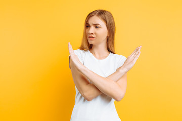 Young serious girl, arms crossed, showing a prohibitive gesture on a yellow background