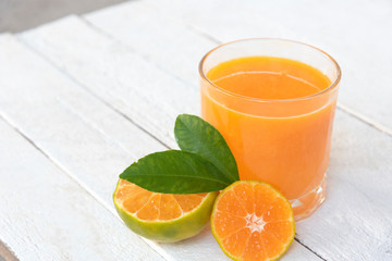 a glass of orange juice and fresh oranges on white wooden base