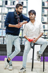 Two indians mans customer buyer at mobile phone store with earphones and wireless speaker listening music. South asian peoples and technologies concept. Cellphone shop.