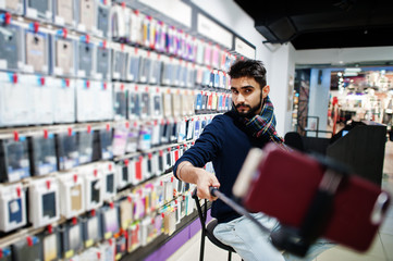 Indian man customer buyer at mobile phone store making selfie by smartphone on monopod stick. South asian peoples and technologies concept. Cellphone shop.