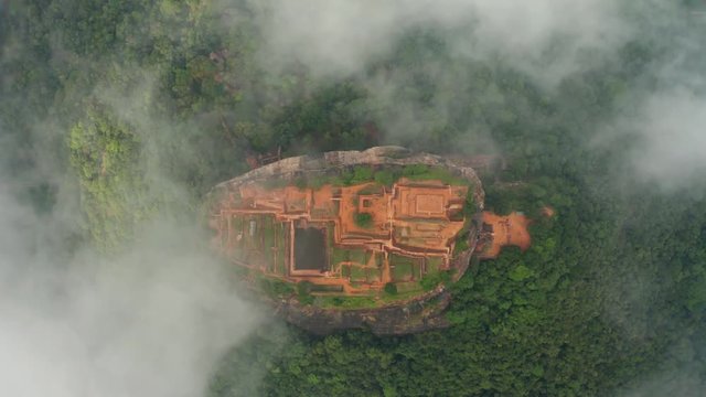 aerial view of the holy mountain Sigiriya. Circling around the mountain through the clouds. Mountain among palm trees and rice fields