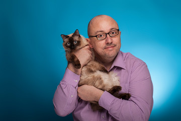 A businessman in a piked shirt holds  a birman cat in the hand