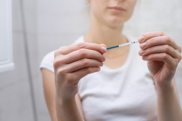 A young attractive woman holds a pregnancy test in her hand. The girl is shocked by the positive...