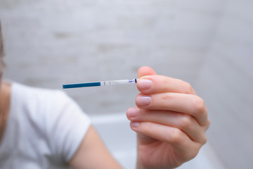 A young attractive woman holds a pregnancy test in her hand. The girl is shocked by the positive result of the pregnancy test. Unwanted pregnancy