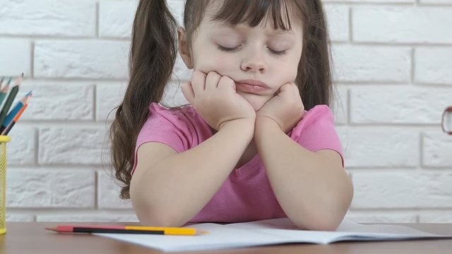 Sad child doing homework. A cute little girl looks at a school notebook. Child learning difficulties concept.
