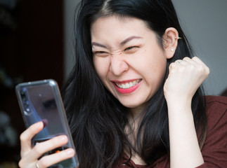 Extremely excited young Asian beautiful woman amazed by mobile app sale message looking at...