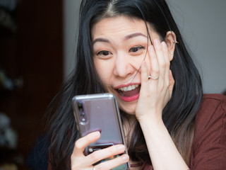 Extremely excited young Asian beautiful woman amazed by mobile app sale message looking at...