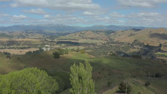 Aerial rise from trees and flax plants to reveal farmlands and Rangitikei ranges, New Zealand 4k