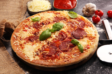 Italian pizza with salami, peperoni - with melted cheese, red tomatoes and green basil on a table decorated by cheese, tomato and cherry tomatoes