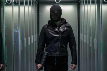 Masked hacker walking through rows of servers