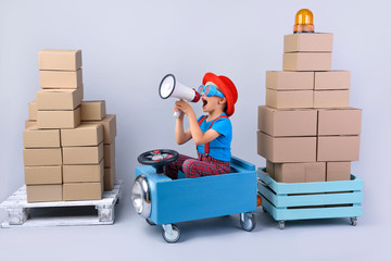 Smiling boy driving blue, fanny car and wagon with small boxes.Happy child with paper boxes on grey background. Studio shot. Delivery, shipping,  transport and supplier concept. 