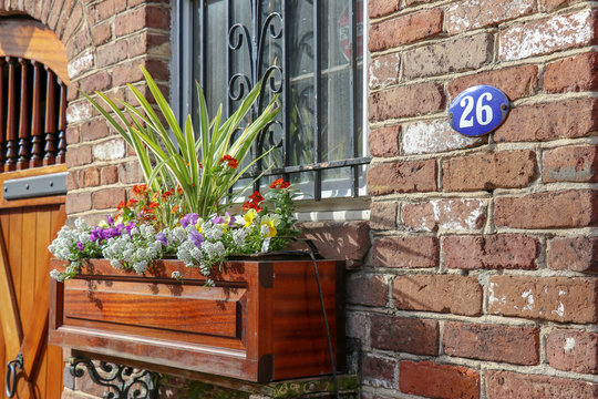 Sunlit colorful flowerbox, doorway, and French blue enamel house number on a brick home in the historic district of Charleston, SC