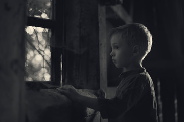 Fototapeta na wymiar A boy looking out the window in the old house, looking for someone, a mysterious scenery, a photo for the cover of the book.