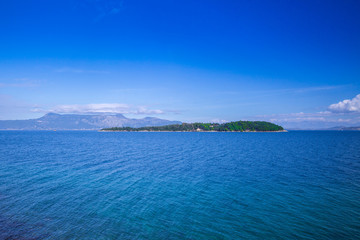 Wonderful romantic summertime panoramic seascape. Sailing yacht with white sails in to the crystal clear azure sea. Small green island against coastline slopes.