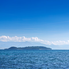 Wonderful romantic summertime panoramic seascape. Sailing yacht with white sails in to the crystal clear azure sea. Small green island against coastline slopes.