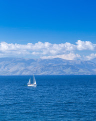 Fototapeta premium Wonderful romantic summertime seascape. Sailing yacht with white sails in to the crystal clear azure sea against coastline slopes.