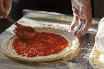 Baker spreads on pizza base on tomato sauce. Pizza production in the restaurant