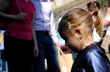 Pensive little girl walking. Parents in the background. Family negative concept. Opposite directions concept.