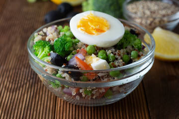 Bowl with quinoa and different vegetables - egg, broccoli, tomato, green peas, red onions. Wooden table. Healthy food.