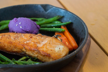 Hot grilled Salmon with mash purple potato and vegetables serve in black plate.