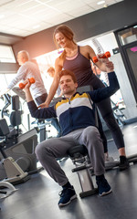 Fit young man and woman in sportswear smiling and lifting dumbells during an exercise class in a gym