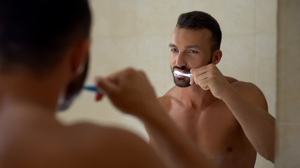 Handsome male brushing teeth in bathroom, every day hygiene, dental care