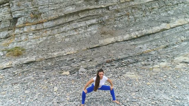 Woman is doing squats the bodyflex on the rock background. Aerial beautiful footage view.