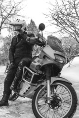 Naklejka premium Rider man is sitting on adventure motorcycle. Winter fun. snowy day. motorbike and snow. black and white. off road dual sport travel tour, active life style concept. winter clothes, vertical photo