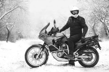 Fototapeta na wymiar Rider man on adventure motorcycle. Winter fun. snowy day. the snow under the wheels of a motorbike. Enduro. off road dual sport travel tour, black and white. winter clothes, equipment