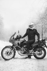 Obraz na płótnie Canvas Rider man is sitting on adventure motorcycle. Winter fun. snowy day. motorbike and snow. black and white. off road dual sport travel tour, active life style concept. winter clothes, vertical photo