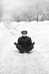 Rider man is sitting on snowy road alone. meditating in the lotus position that used to end the winter, active life style concept. winter clothes, equipment, vertical photo, back and white