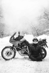 Fototapeta na wymiar Rider man and adventure motorcycle. snowy day. meditating in the lotus position that used to end the winter. travel tour, back and white. winter clothes, equipment, vertical photo