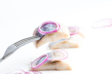piece of herring with a purple onion ring on a fork. White background