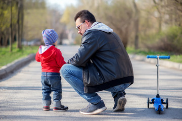 Young father squatted down in the street to talk to his toddler son during walk outdoor. View from...