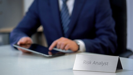 Serious risk analyst working on tablet computer, counting new project chances
