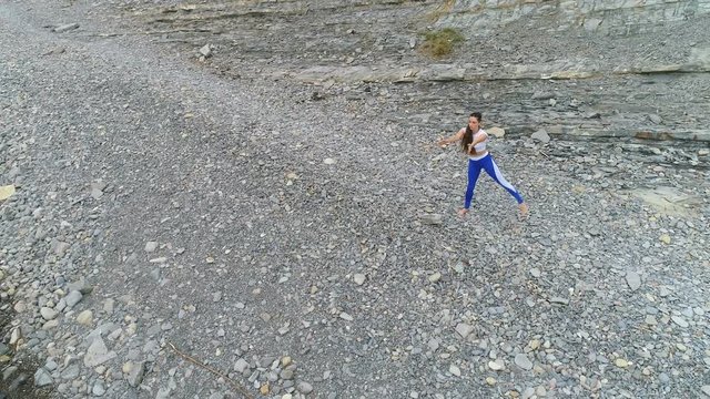 Girl is doing exercise for legs the bodyflex during breathing exercises on the sea and rock background. Aerial video.