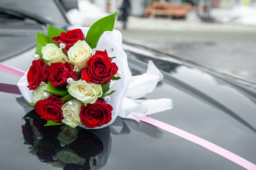 Closeup wedding bouquet on black car cowl with pink ribbon, street on background