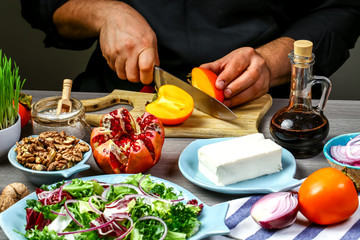 Chef hands cooking Tasty Persimmon salad with arugula, nuts, feta cheese, Fitness food. Superfoods